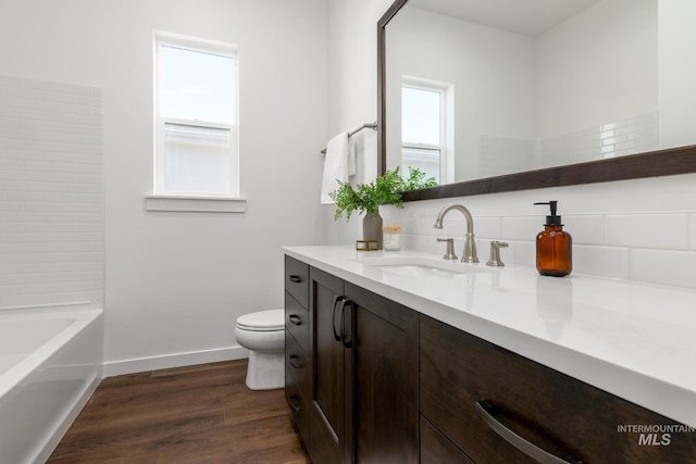 bathroom featuring backsplash, toilet, vanity, wood finished floors, and baseboards
