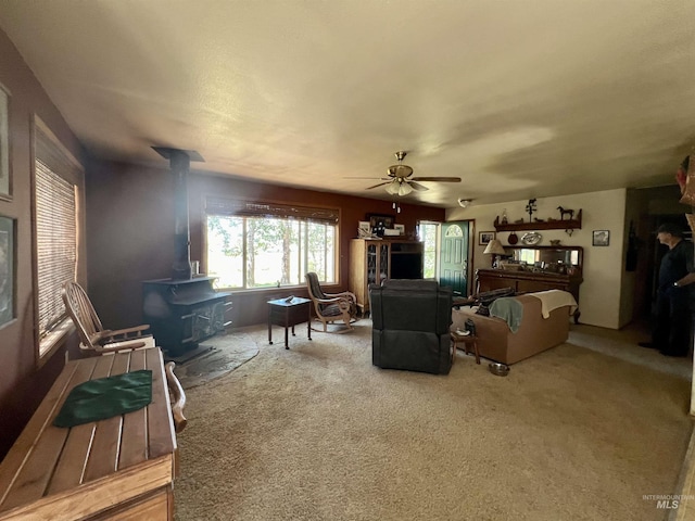 living room featuring ceiling fan, carpet flooring, and a wood stove