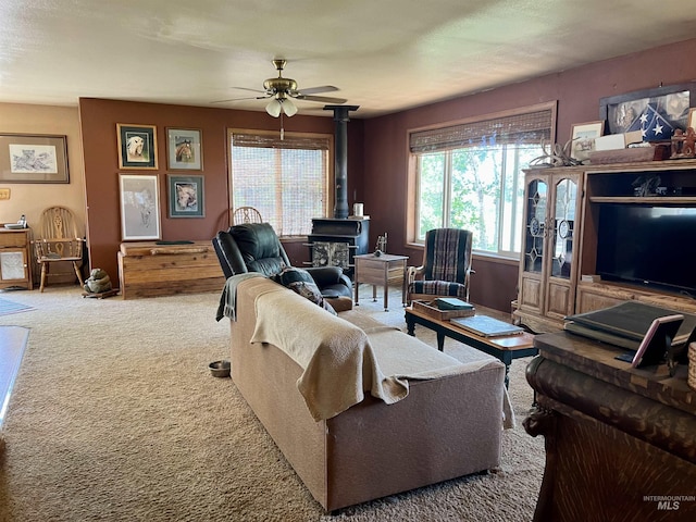 living room featuring a wood stove, ceiling fan, and light carpet