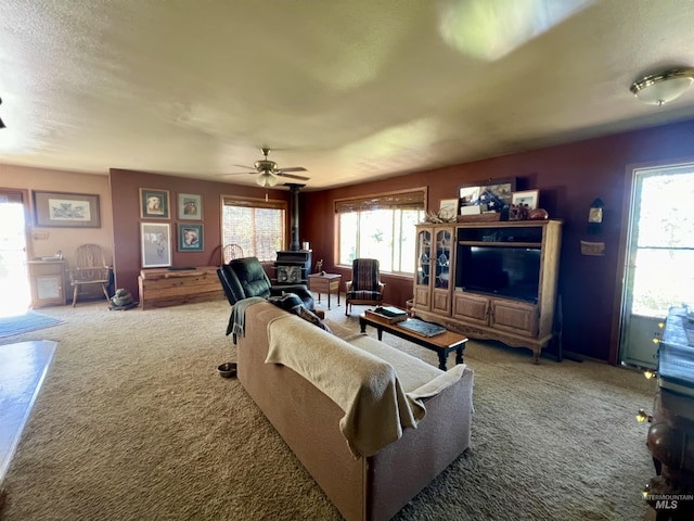 carpeted living room featuring ceiling fan and a wood stove