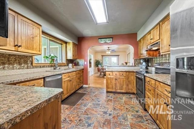 kitchen featuring arched walkways, stainless steel appliances, backsplash, a peninsula, and under cabinet range hood