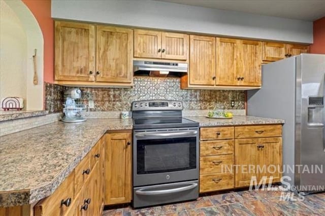 kitchen with arched walkways, appliances with stainless steel finishes, brown cabinets, under cabinet range hood, and backsplash