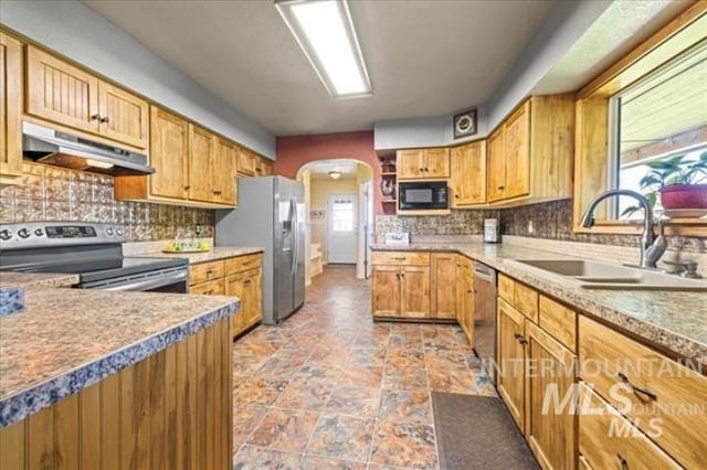 kitchen featuring arched walkways, under cabinet range hood, a sink, a healthy amount of sunlight, and appliances with stainless steel finishes