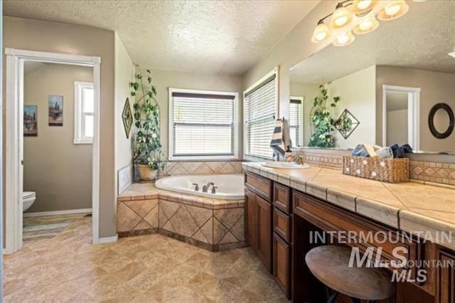 bathroom featuring a textured ceiling, a garden tub, toilet, vanity, and baseboards