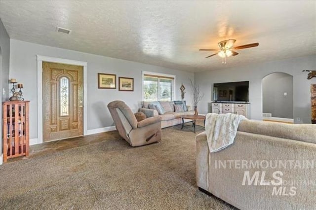 carpeted living room featuring a ceiling fan, visible vents, arched walkways, and a textured ceiling