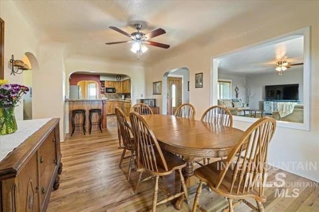 dining area with ceiling fan, arched walkways, and light wood-style flooring