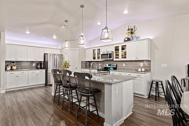 kitchen featuring tasteful backsplash, a center island with sink, lofted ceiling, and appliances with stainless steel finishes