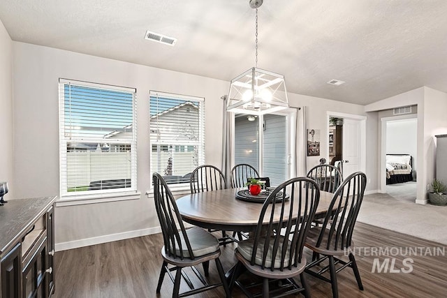 dining space with a textured ceiling, vaulted ceiling, dark wood-type flooring, and an inviting chandelier