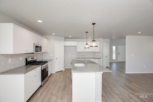 kitchen featuring sink, decorative light fixtures, stainless steel appliances, a kitchen island with sink, and white cabinets