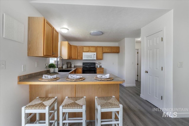 1471 Wrangler St, Twin Falls, ID 83301 - kitchen featuring a sink, black range with electric cooktop, white microwave, a peninsula, and dark wood-style floors