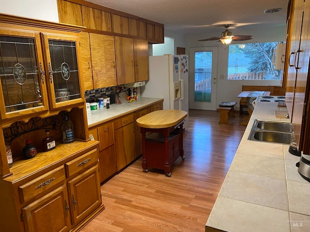 kitchen with a textured ceiling, white refrigerator with ice dispenser, sink, light hardwood / wood-style flooring, and ceiling fan