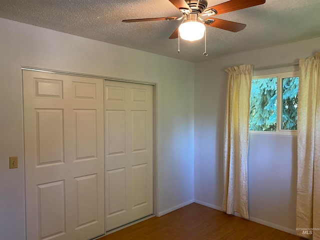 unfurnished bedroom featuring a closet, ceiling fan, wood-type flooring, and a textured ceiling