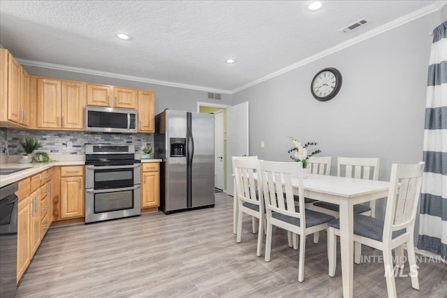 kitchen with light brown cabinetry, tasteful backsplash, ornamental molding, stainless steel appliances, and light wood-type flooring