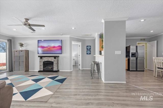 living room featuring light hardwood / wood-style flooring, a fireplace, ornamental molding, and a textured ceiling