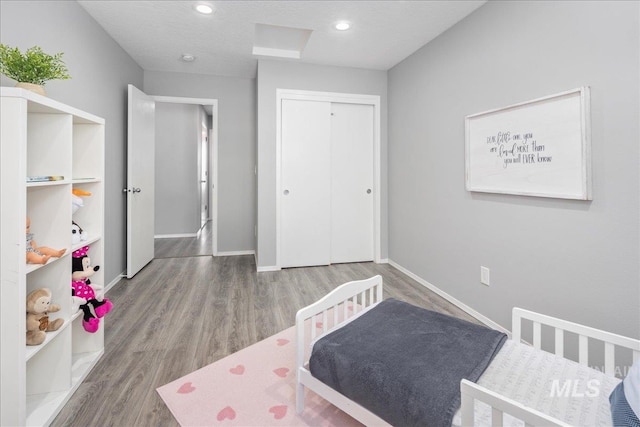 bedroom featuring a crib, hardwood / wood-style floors, a textured ceiling, and a closet