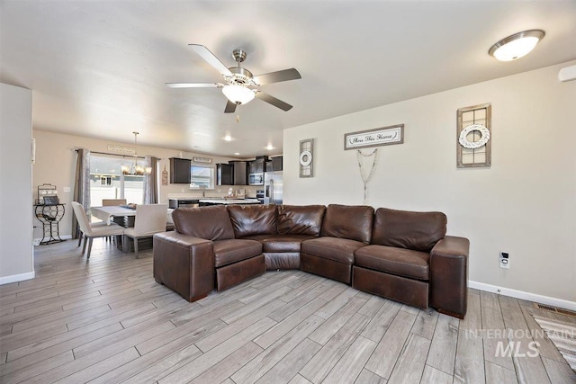 living room featuring light wood-style flooring, baseboards, and ceiling fan with notable chandelier