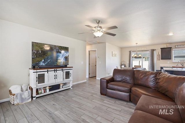 living area featuring ceiling fan with notable chandelier, light wood-type flooring, and baseboards