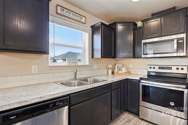 kitchen with light wood-style flooring, stainless steel appliances, a sink, light countertops, and dark brown cabinets