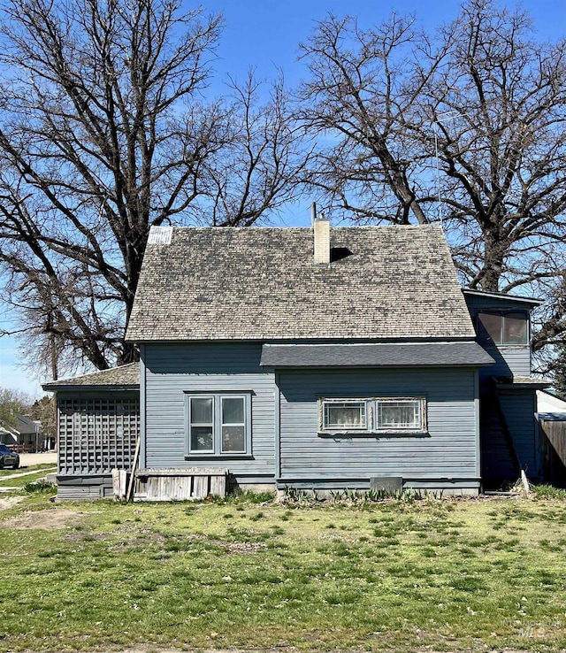 rear view of property featuring roof with shingles, a yard, and a chimney