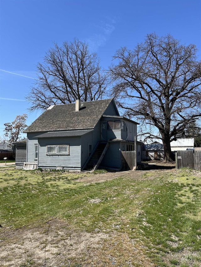 view of home's exterior with a chimney, roof with shingles, fence, and a yard