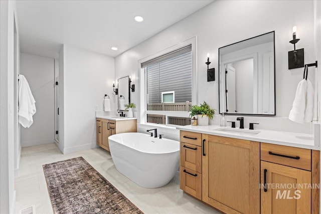 bathroom with a freestanding tub, two vanities, a sink, and recessed lighting