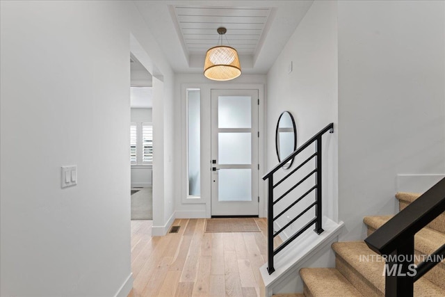 foyer featuring visible vents, baseboards, stairs, light wood-style floors, and a tray ceiling