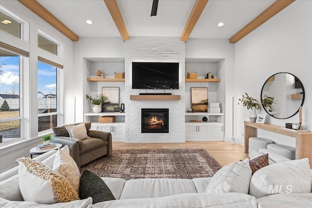 living area featuring built in shelves, beam ceiling, a fireplace, recessed lighting, and light wood-style floors