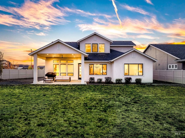 back of property at dusk with stucco siding, a yard, fence, and a patio