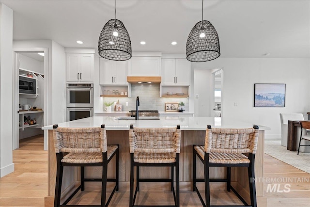 kitchen featuring a kitchen island with sink, stainless steel appliances, white cabinets, light countertops, and pendant lighting