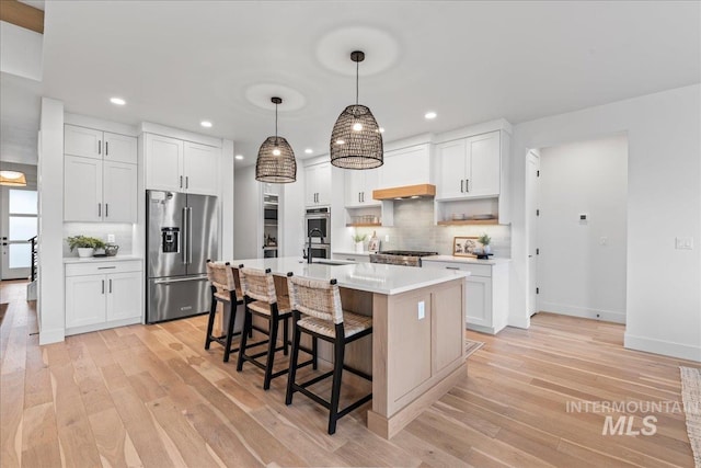 kitchen with stainless steel appliances, light countertops, a center island with sink, and white cabinetry