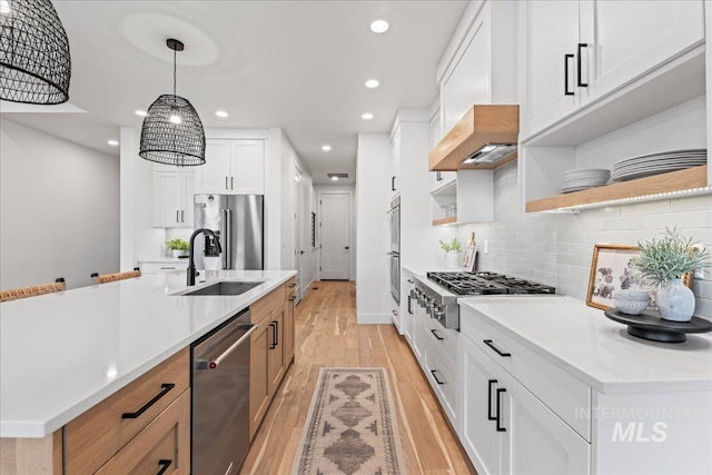 kitchen featuring stainless steel appliances, a sink, white cabinetry, light countertops, and open shelves