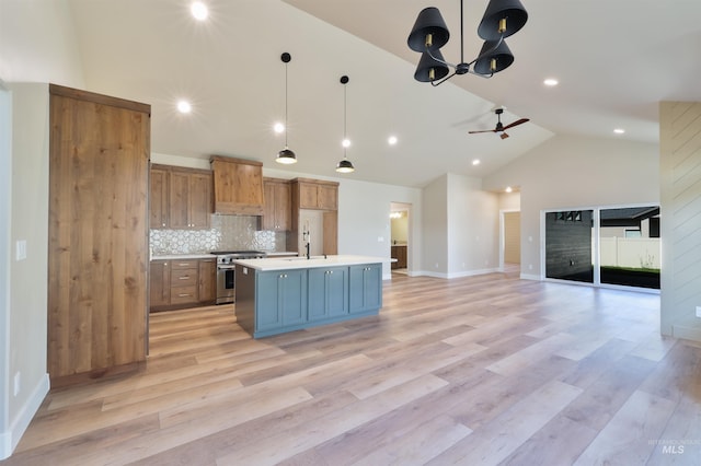 kitchen with a kitchen island with sink, open floor plan, hanging light fixtures, light countertops, and high end stainless steel range oven