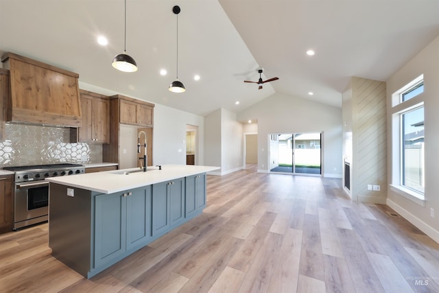 kitchen featuring decorative light fixtures, open floor plan, light countertops, stainless steel range, and a center island with sink