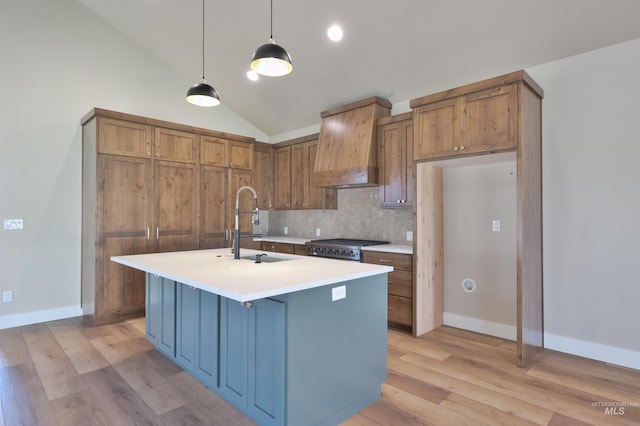 kitchen with brown cabinets, a center island with sink, light countertops, hanging light fixtures, and premium range hood