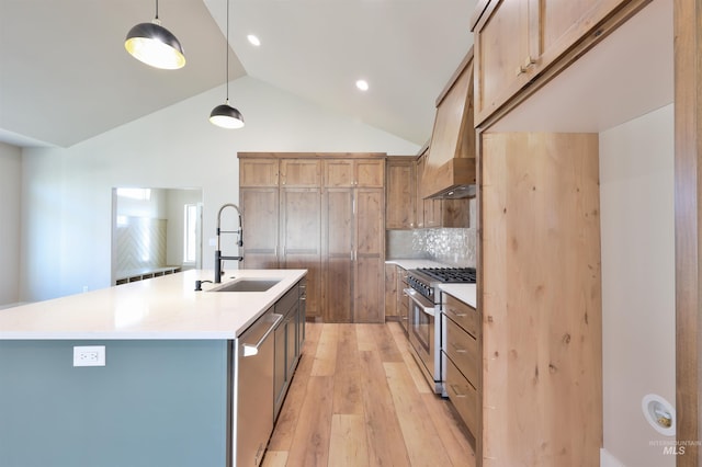 kitchen featuring an island with sink, stainless steel appliances, light countertops, pendant lighting, and a sink