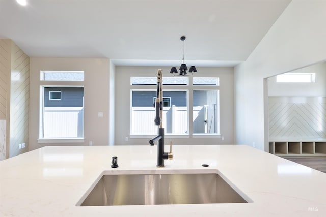 kitchen with a notable chandelier, a sink, light stone countertops, and pendant lighting