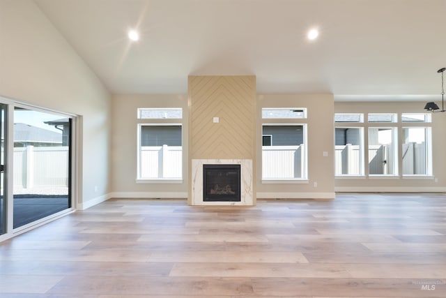 unfurnished living room with light wood finished floors, baseboards, vaulted ceiling, a fireplace, and recessed lighting