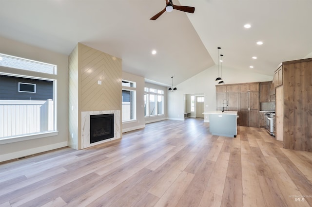 unfurnished living room featuring a fireplace, light wood-style flooring, a ceiling fan, a sink, and high vaulted ceiling