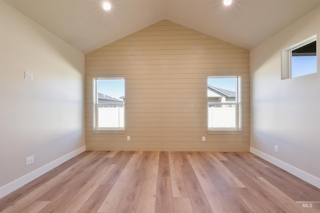 empty room with lofted ceiling, light wood-style flooring, and baseboards