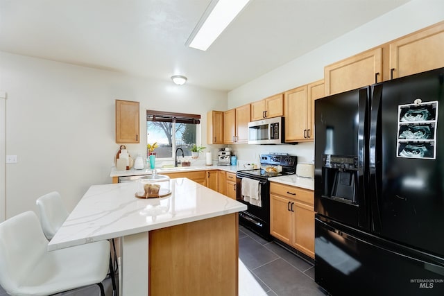 kitchen featuring sink, dark tile patterned flooring, a kitchen breakfast bar, a center island, and black appliances