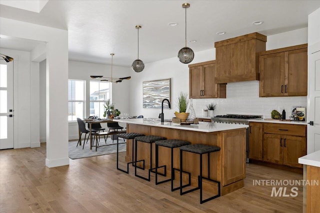 kitchen with an island with sink, hardwood / wood-style flooring, hanging light fixtures, backsplash, and custom range hood