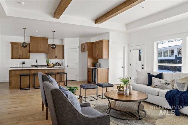 living room featuring beamed ceiling, sink, and light hardwood / wood-style floors