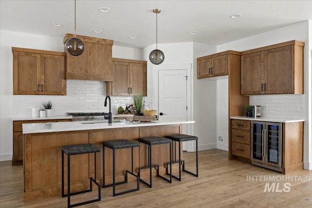 kitchen featuring a center island with sink, hanging light fixtures, wine cooler, light hardwood / wood-style floors, and sink