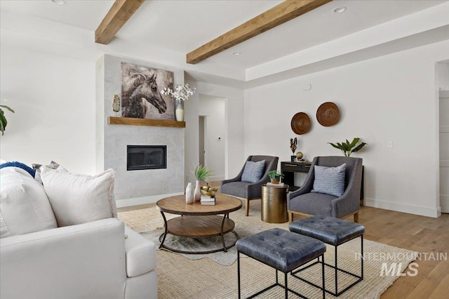 living room with a tiled fireplace, beamed ceiling, and wood-type flooring