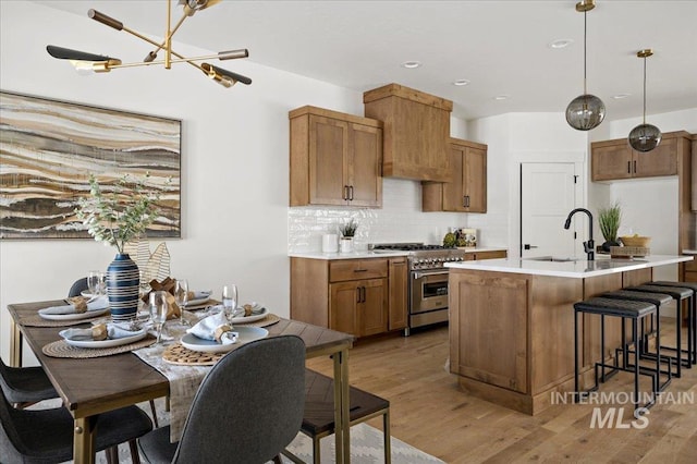 kitchen featuring hanging light fixtures, stainless steel stove, decorative backsplash, sink, and a kitchen island with sink