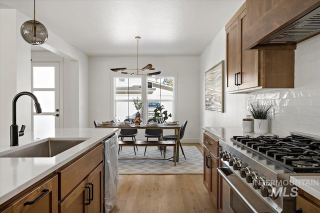 kitchen featuring stovetop, premium range hood, light hardwood / wood-style floors, pendant lighting, and sink