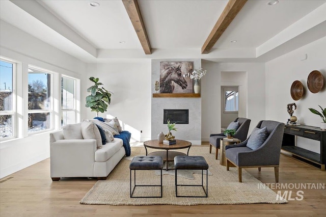 living room with beamed ceiling, a large fireplace, and light hardwood / wood-style floors