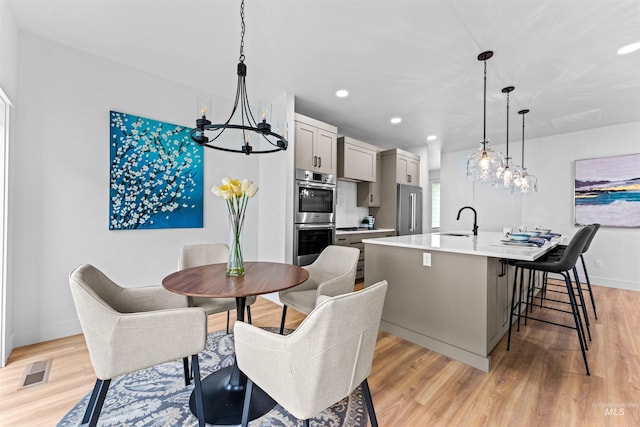 dining area featuring sink, light hardwood / wood-style floors, and a notable chandelier