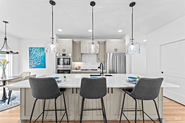 kitchen with stainless steel appliances, light hardwood / wood-style floors, a kitchen breakfast bar, sink, and pendant lighting