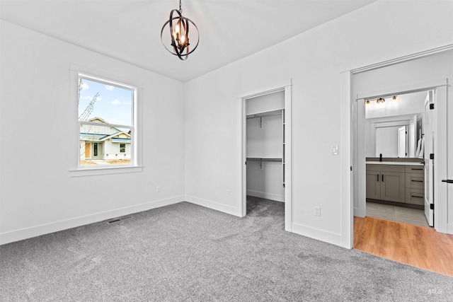 unfurnished bedroom featuring an inviting chandelier, connected bathroom, light carpet, and a walk in closet